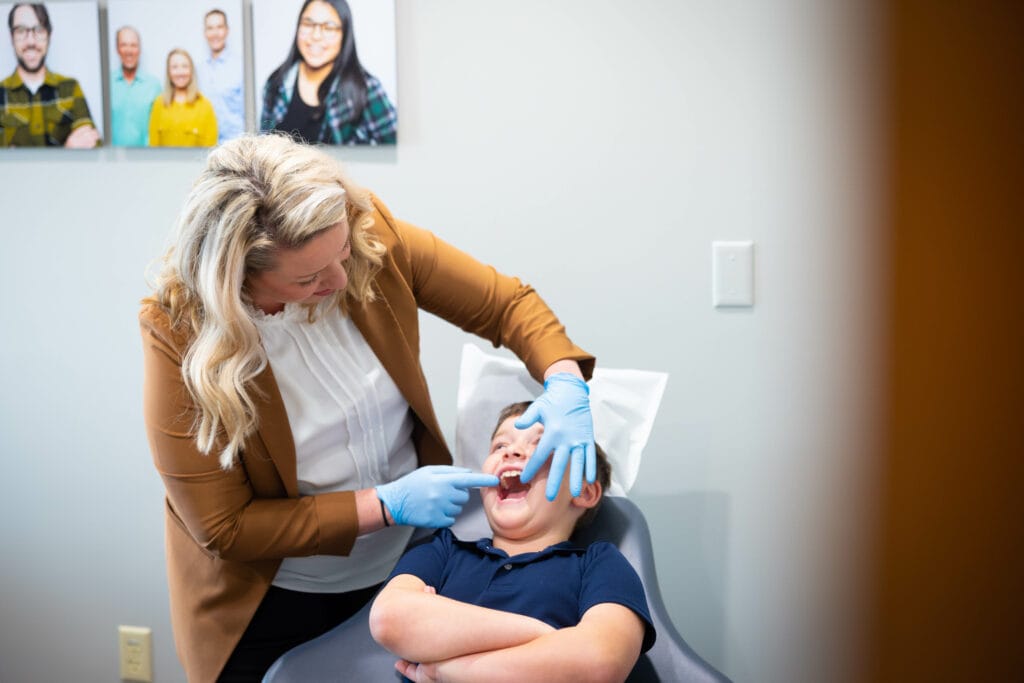 An orthodontist examines a smiling child’s teeth.