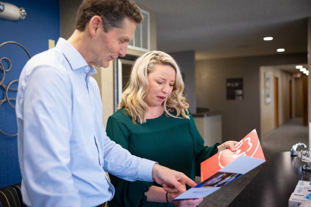 An orthodontist and woman review brochures at a counter.